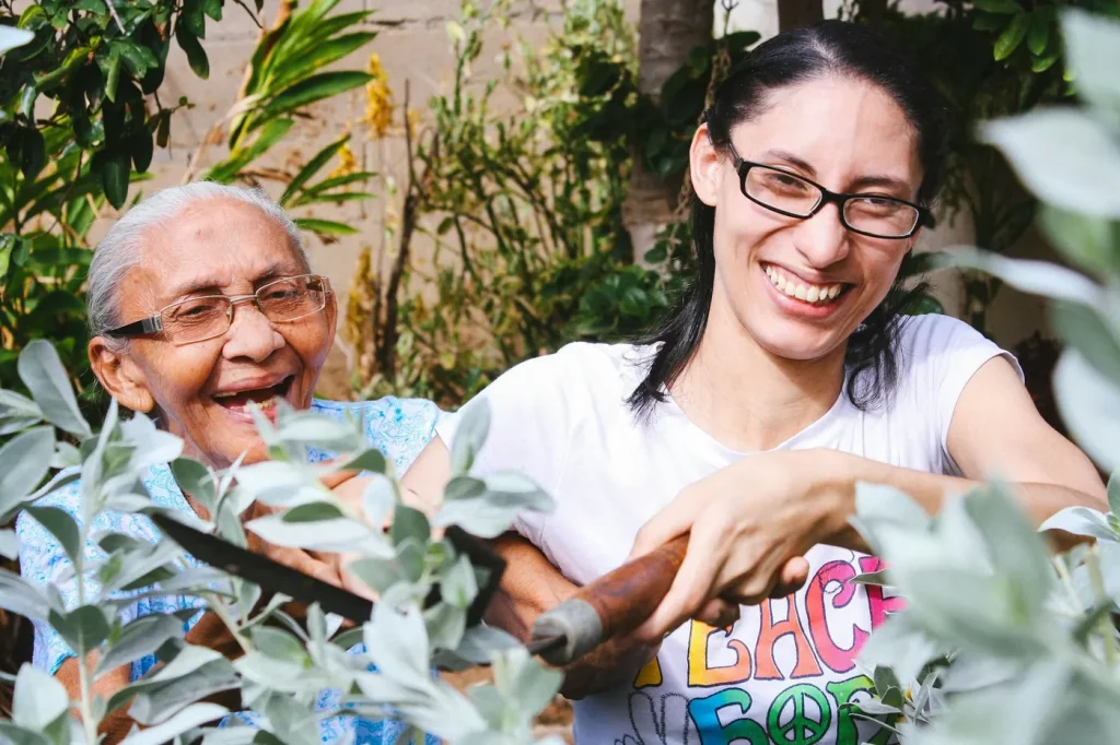 An older woman laughs as she works in the garden alongside a younger woman