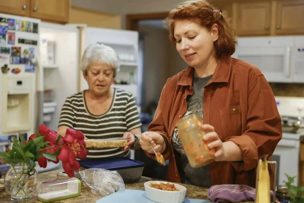 An older woman and a younger woman prepare a meal together at the kitchen bench